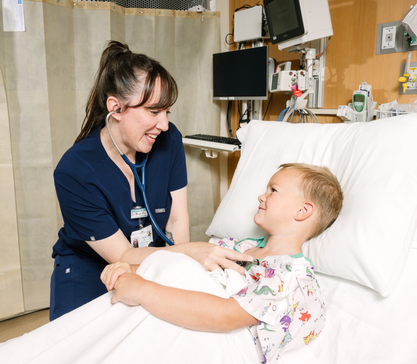 photo of nurse in blue scrubs with stethoscope listening to small child